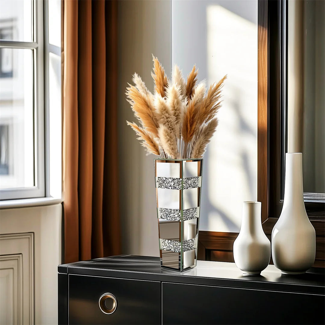 Decorative vase with dried pampas grass on a table next to a window.