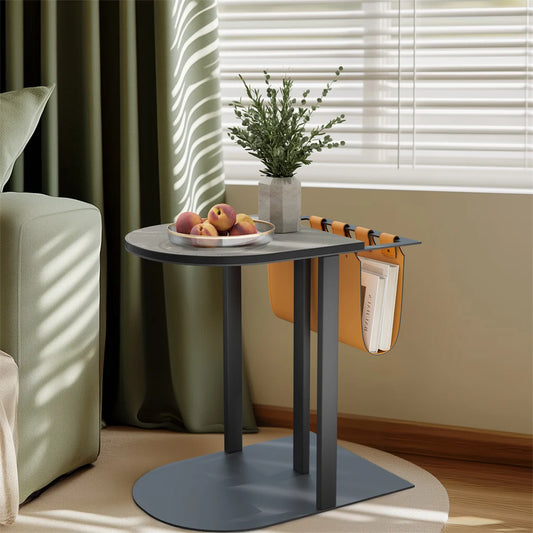 Small round table with a plant, fruits, and a bag in a living room setting.