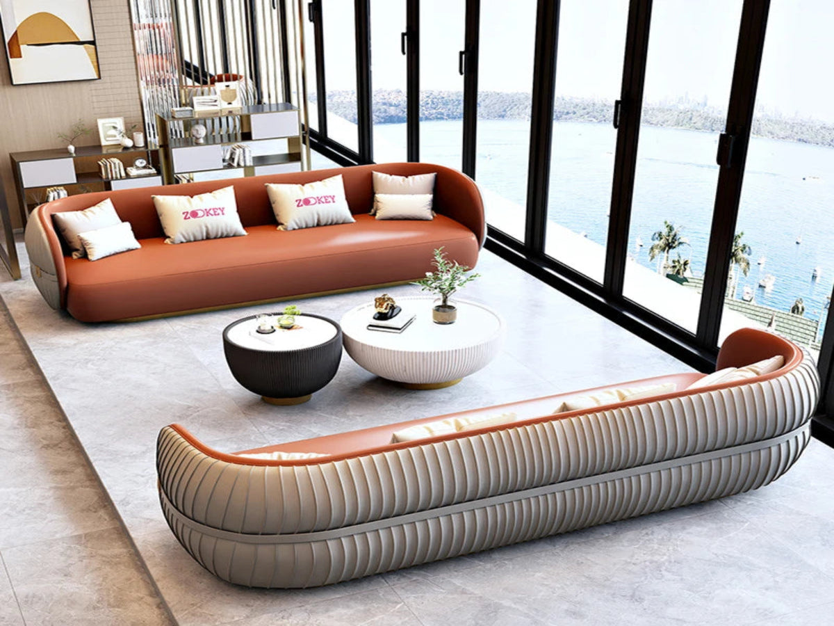 Modern living room with a brown sofa and a curved beige sofa in front of large windows with a view of water.