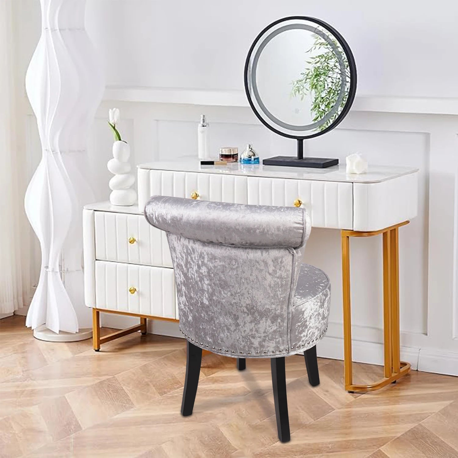 White vanity table with gold legs and a round mirror, accompanied by a gray velvet chair.