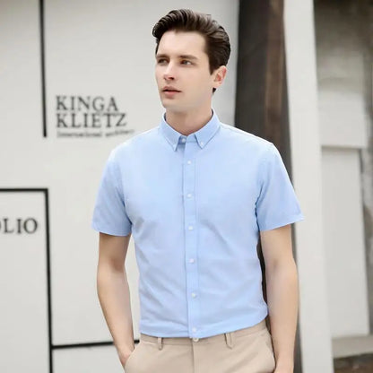 Man wearing a light blue short-sleeve shirt standing in front of a branded wall.