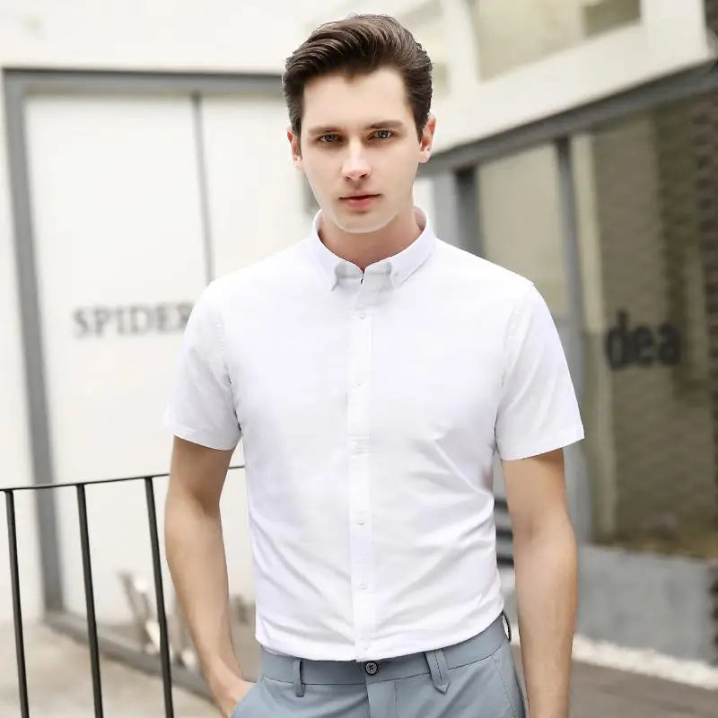 Man wearing a white short-sleeve shirt and gray pants standing outdoors.