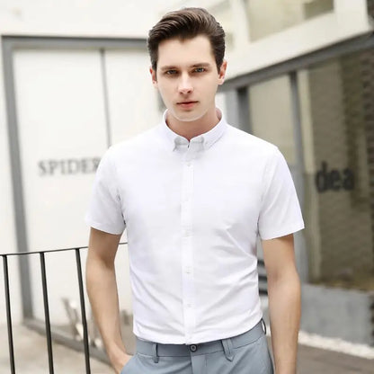 Man wearing a white short-sleeve shirt and gray pants standing outdoors.