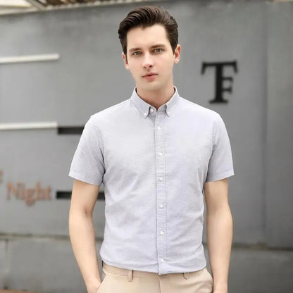 Man wearing a light gray short-sleeve shirt standing in front of a gray wall with a logo.