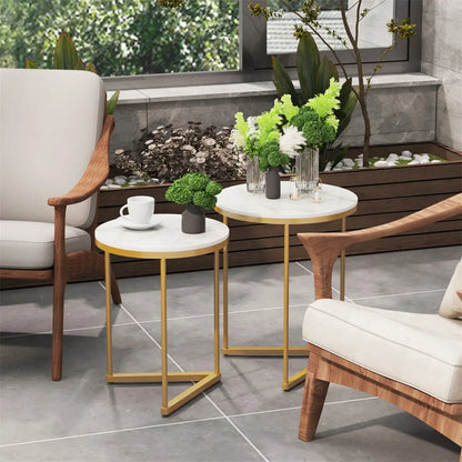Outdoor setting with wooden chairs, white cushions, and small round tables with gold legs on a patio.