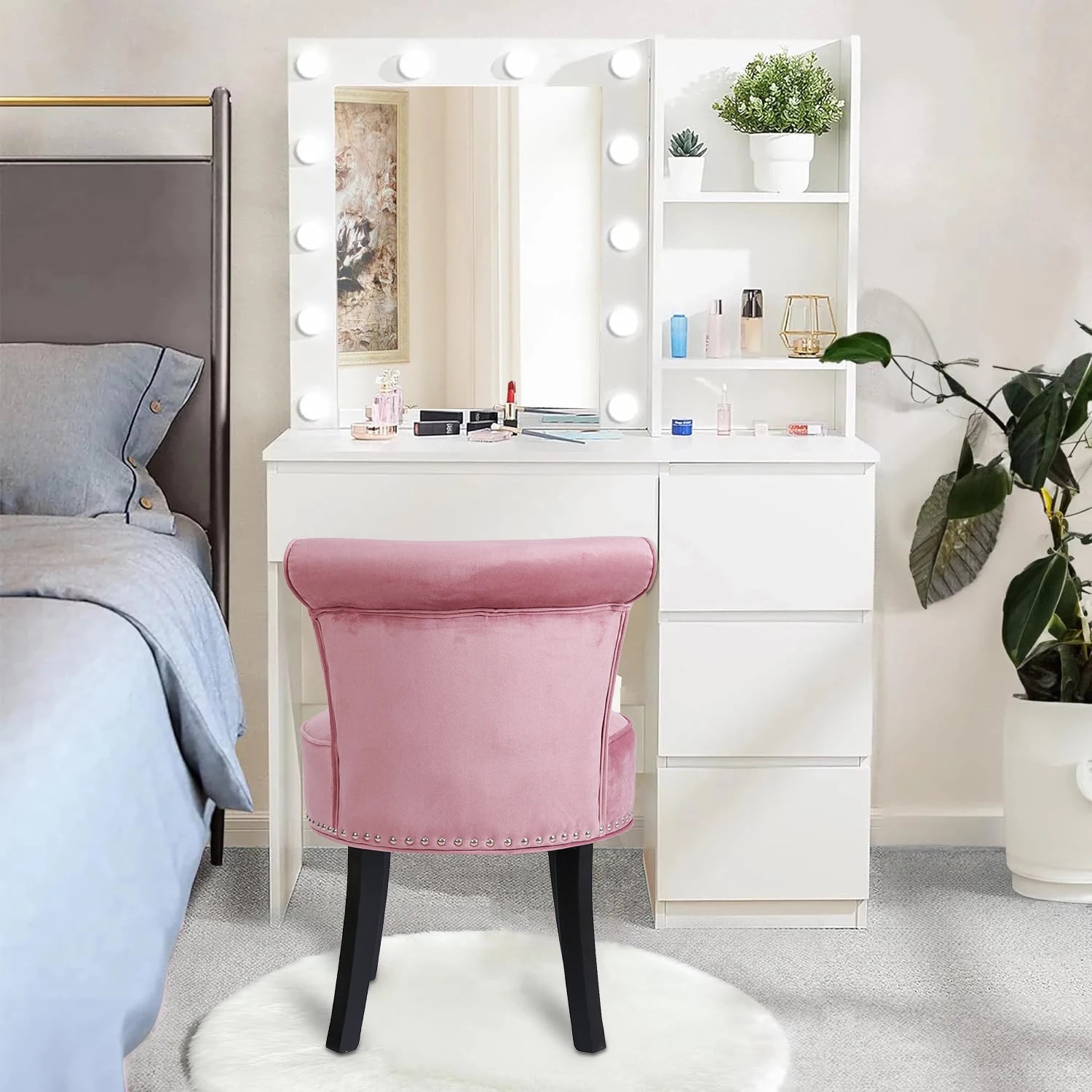 White vanity table with mirror and lights, pink chair, and cosmetic products in a bedroom setting.